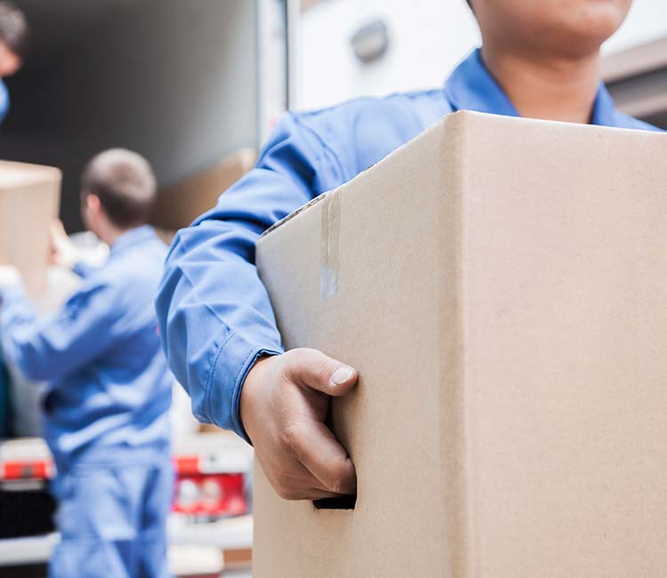 A mover in blue uniform carrying a cardboard box.