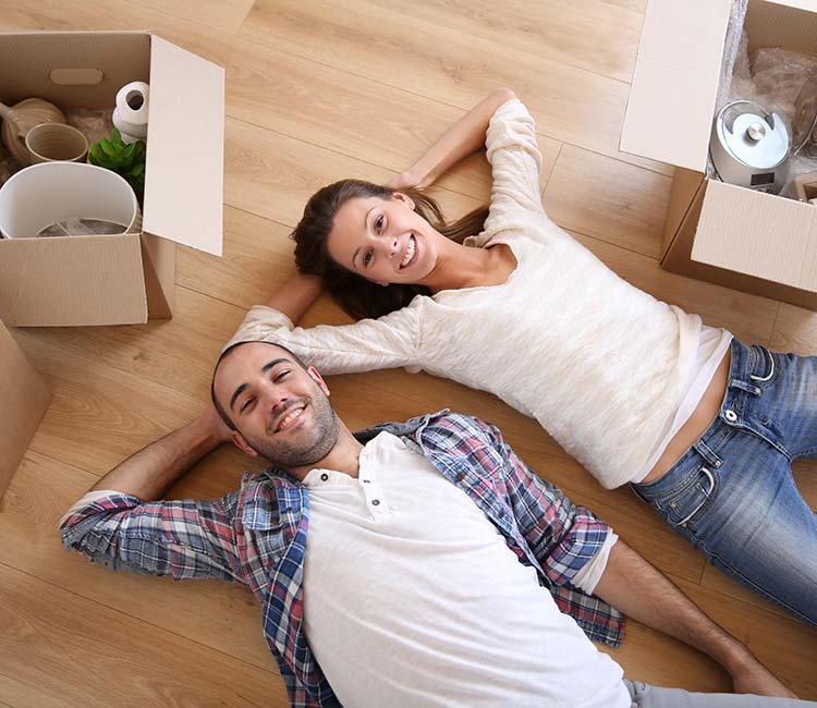 A happy couple lying on the floor surrounded by moving boxes.