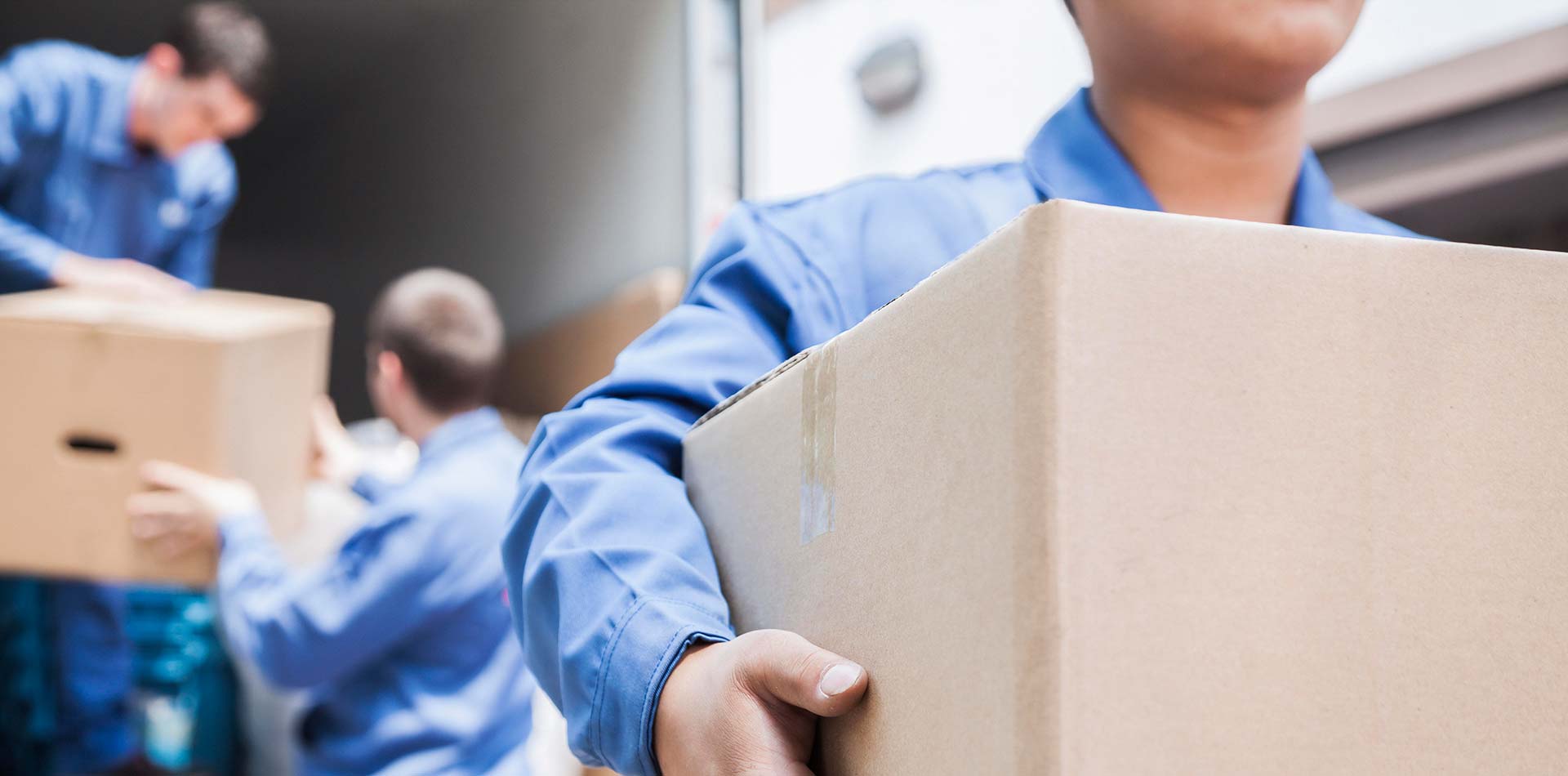 A mover in blue uniform carrying a cardboard box.