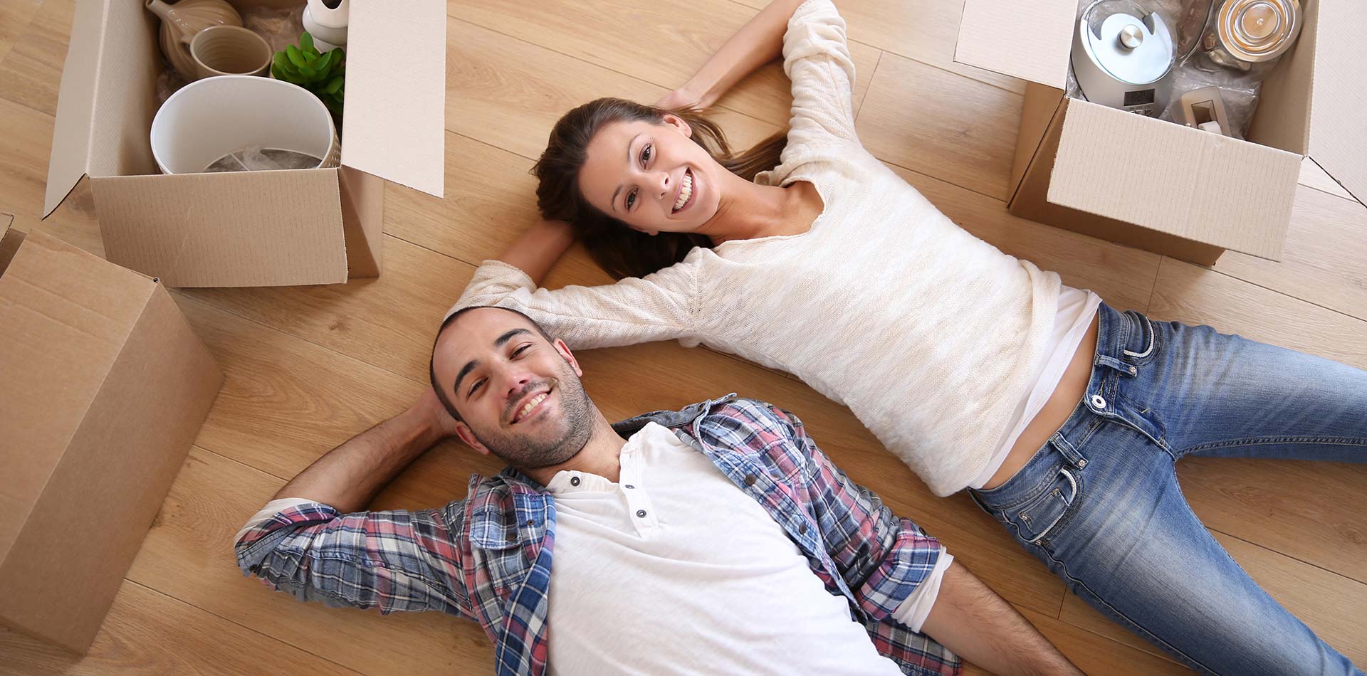 A happy couple lying on the floor surrounded by moving boxes.