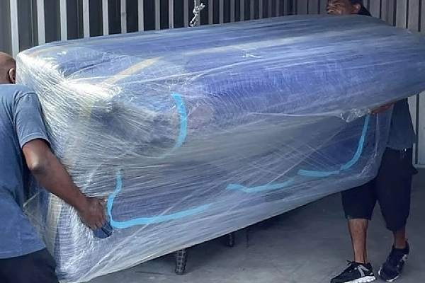 Professional movers handling a large, wrapped sofa in Sarasota.